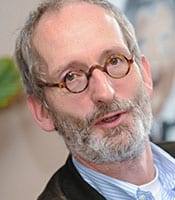 Peter Pappert Ein Mann mittleren Alters mit Brille, grauem Bart und kurzen Haaren blickt leicht an der Kamera vorbei. Er trägt ein hellblaues Hemd und eine dunkle Jacke. Der Hintergrund ist leicht unscharf.